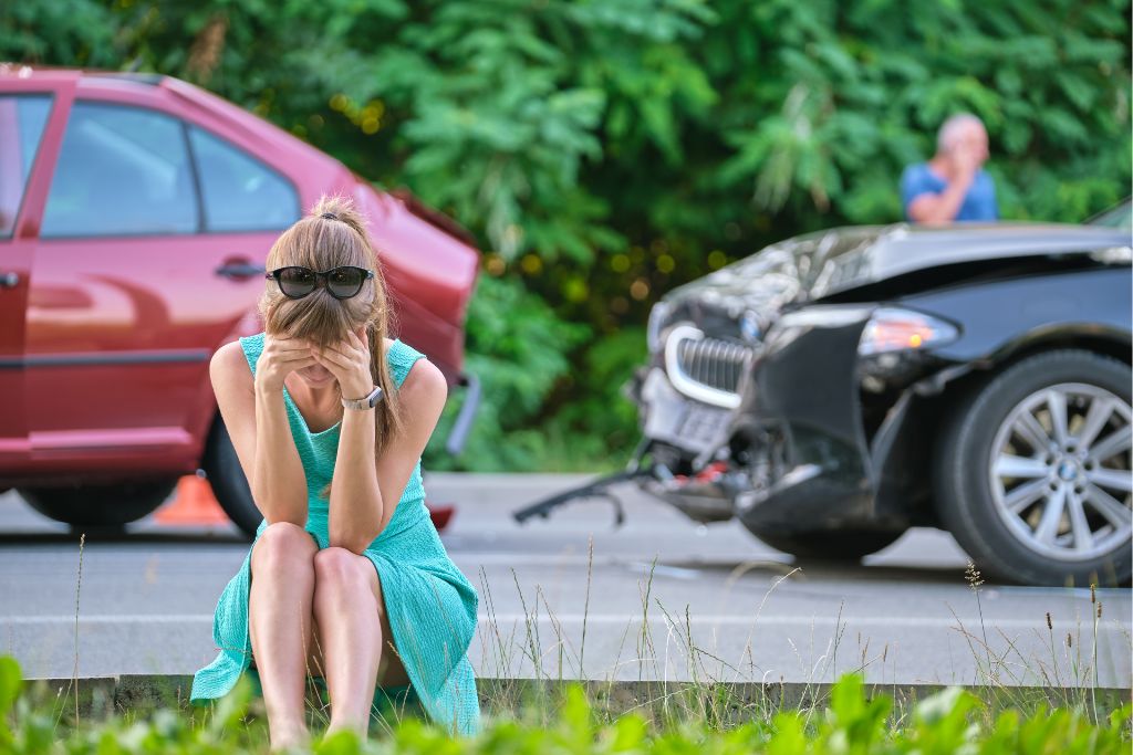 woman sitting in front of a car accident with her head in her hands