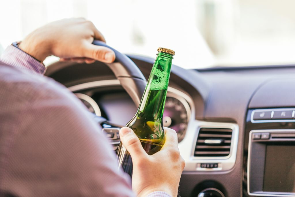 man driving a car with a beer in his right hand