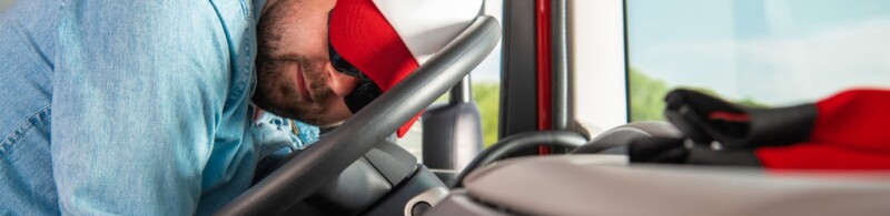 A truck driver asleep with his head on the steering wheel.