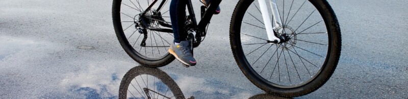 The lower half of a bicycle being pedaled by someone on a wet surface.