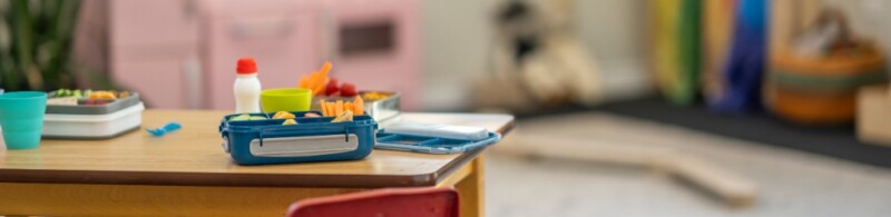 An unoccupied school desk with a book and food.