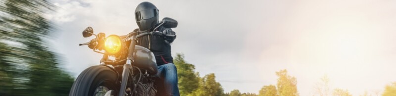 A helmeted man riding a motorcycle on the road with his head light on.