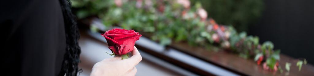 hand holding a red flower over a casket