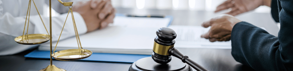 A mans hads clasped together ontop of desk discussing legal documents with another man.